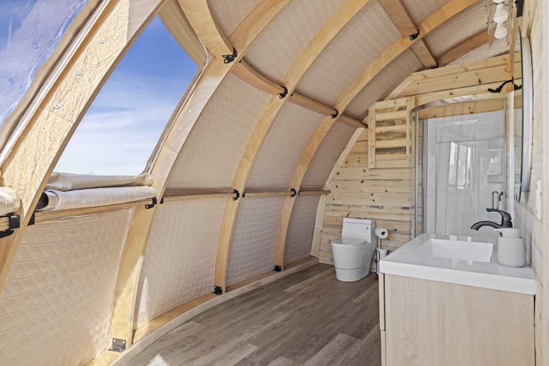 Alt text: "Interior view of a stylish geodesic dome with wooden accents, featuring a modern bathroom setup. Ideal for luxury glamping or as a sustainable living space. Keywords: geodesic dome house, glamping pods for sale, dome home, luxury Airbnb."