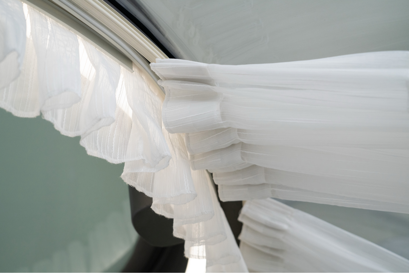 Alt text: &quot;Close-up of white curtains inside a geodesic dome with porthole windows, showcasing the elegant interior design of a luxury glamping pod. Ideal for sustainable living and stylish outdoor accommodations.&quot;